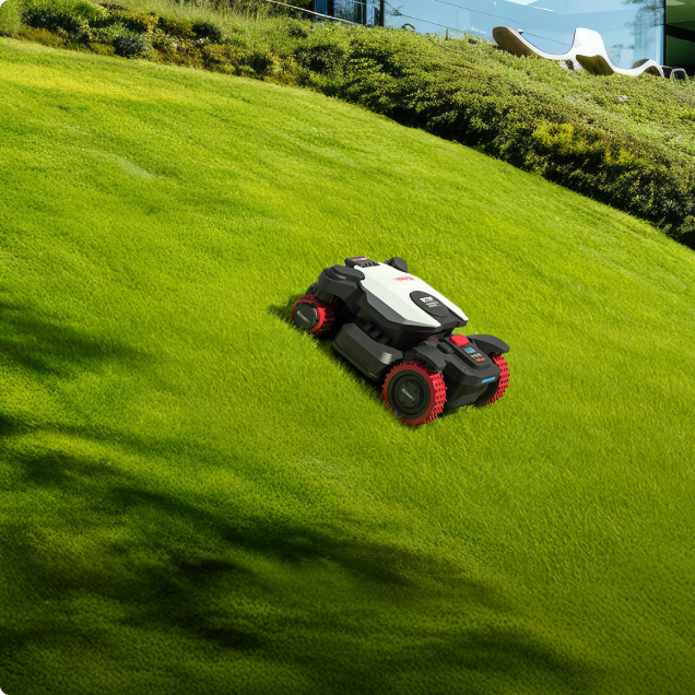 Robotic lawn mower on a grassy hillside with a modern house in the background